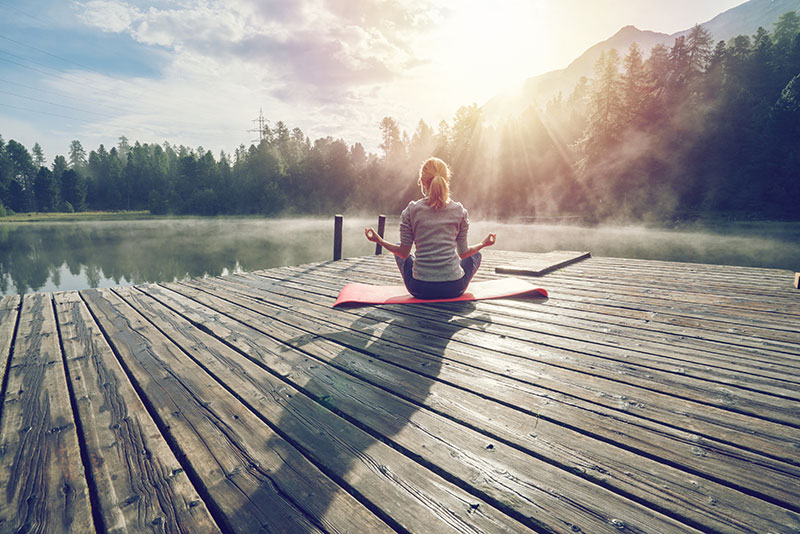 woman doing yoga on a dock by a lake