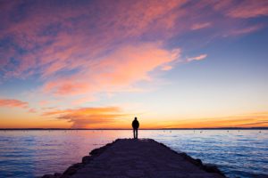 person silhouette at sunset looking over water